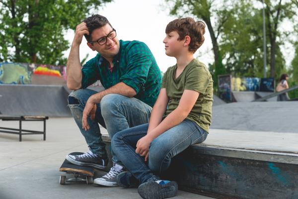 Older male sitting with younger boy in a skate park with skateboards